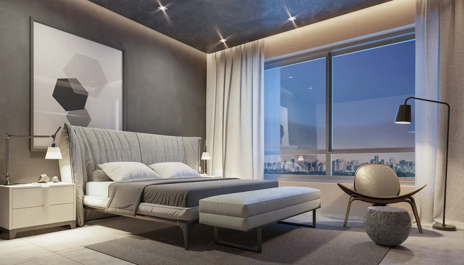 Uma suíte mobiliada: a cama com cabeceira cinza estofada, a poltrona de madeira, a luminária de pé, um quadro com hexágonos e a janela para a cidade ao entardecer.