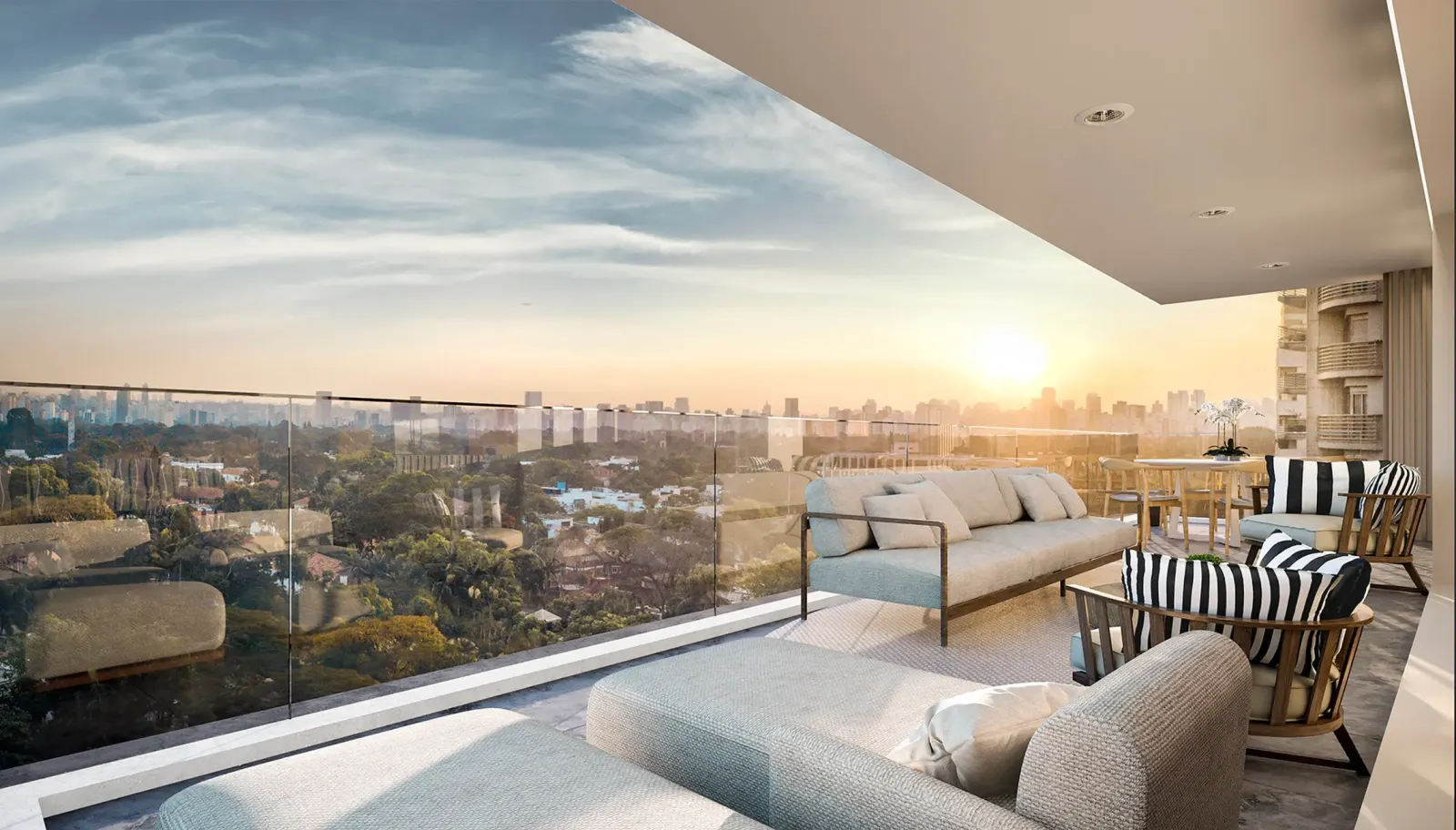 A varanda mobiliada ao pôr do sol: os sofás claros, as poltronas listradas, o guarda-corpo de vidro e o verde dos Jardins até o horizonte.
