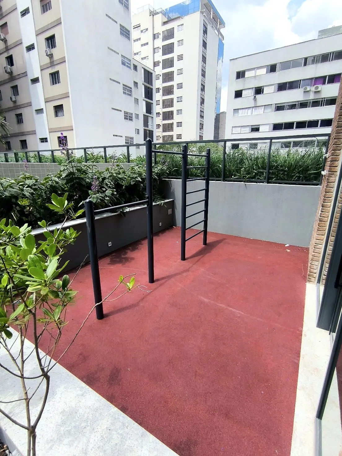 O espaço funcional ao ar livre: o piso de borracha vermelha, as barras de exercício e os canteiros em volta.