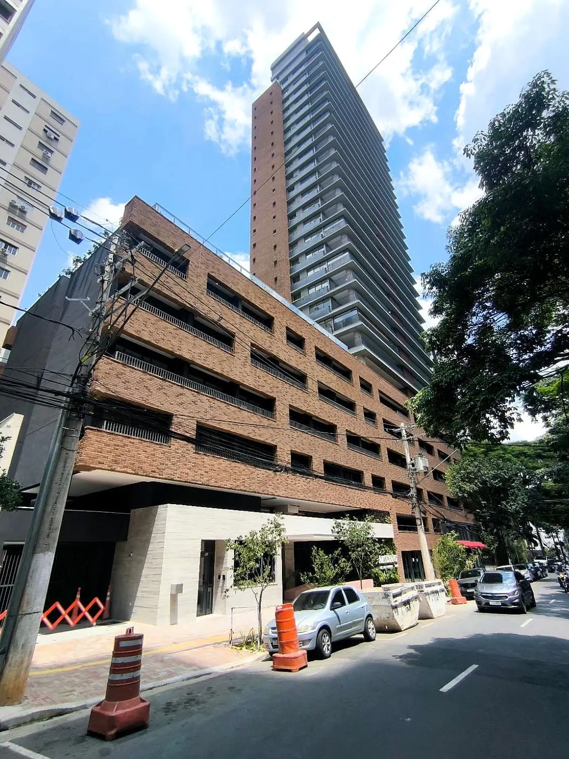 A torre vista de baixo, pela Rua Sampaio Viana: a base larga de tijolo com varandas, a torre alta acima e as árvores da rua.