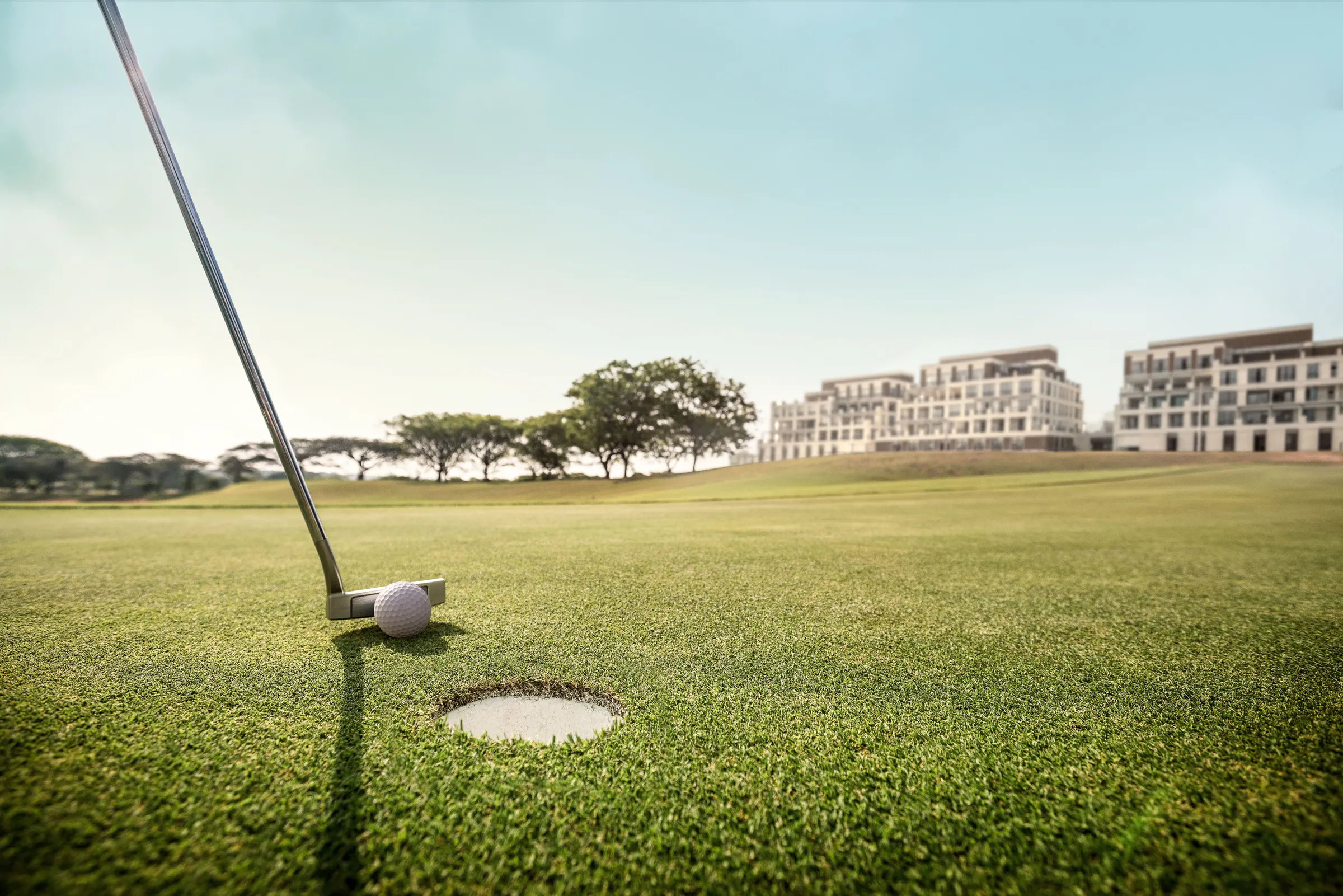 Bola de golfe junto ao buraco no gramado do campo de Rees Jones, com os edifícios residenciais ao fundo.