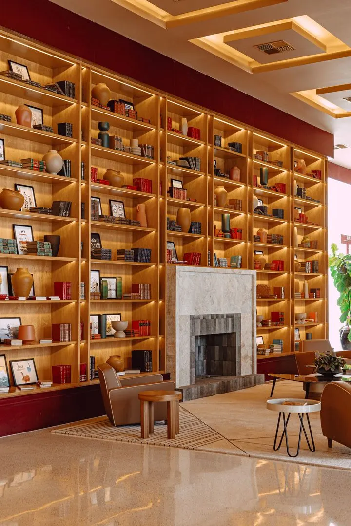 O lobby das Golf Residences: estante de madeira do piso ao teto, lareira de mármore e poltronas.