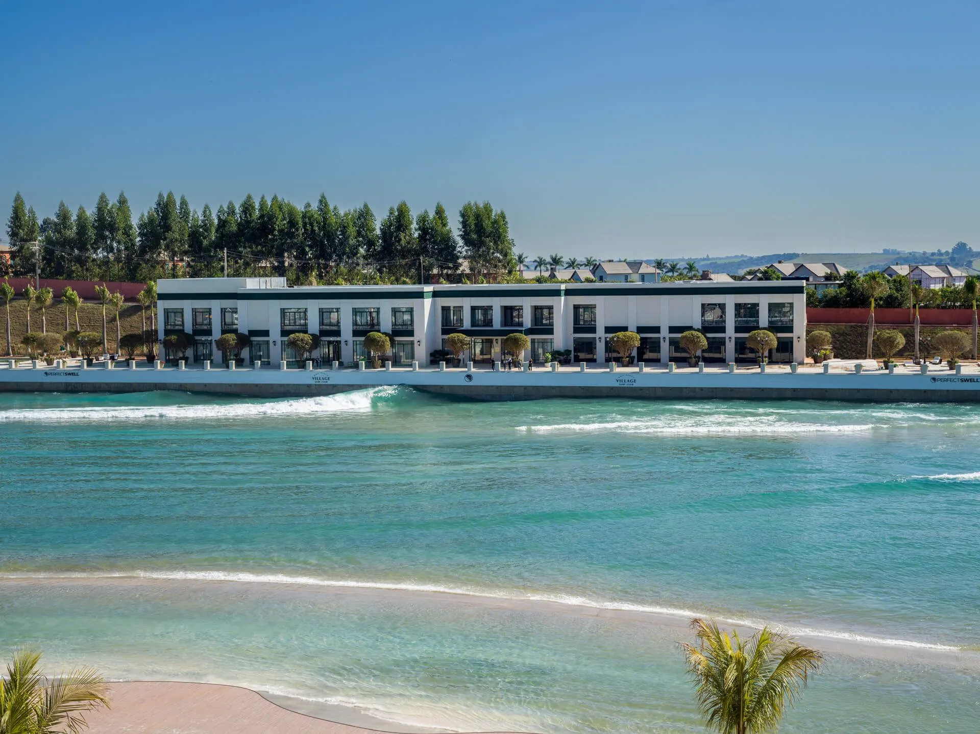 A praia da piscina de ondas do Boa Vista Village, com a água turquesa em primeiro plano e o clube à beira da areia.