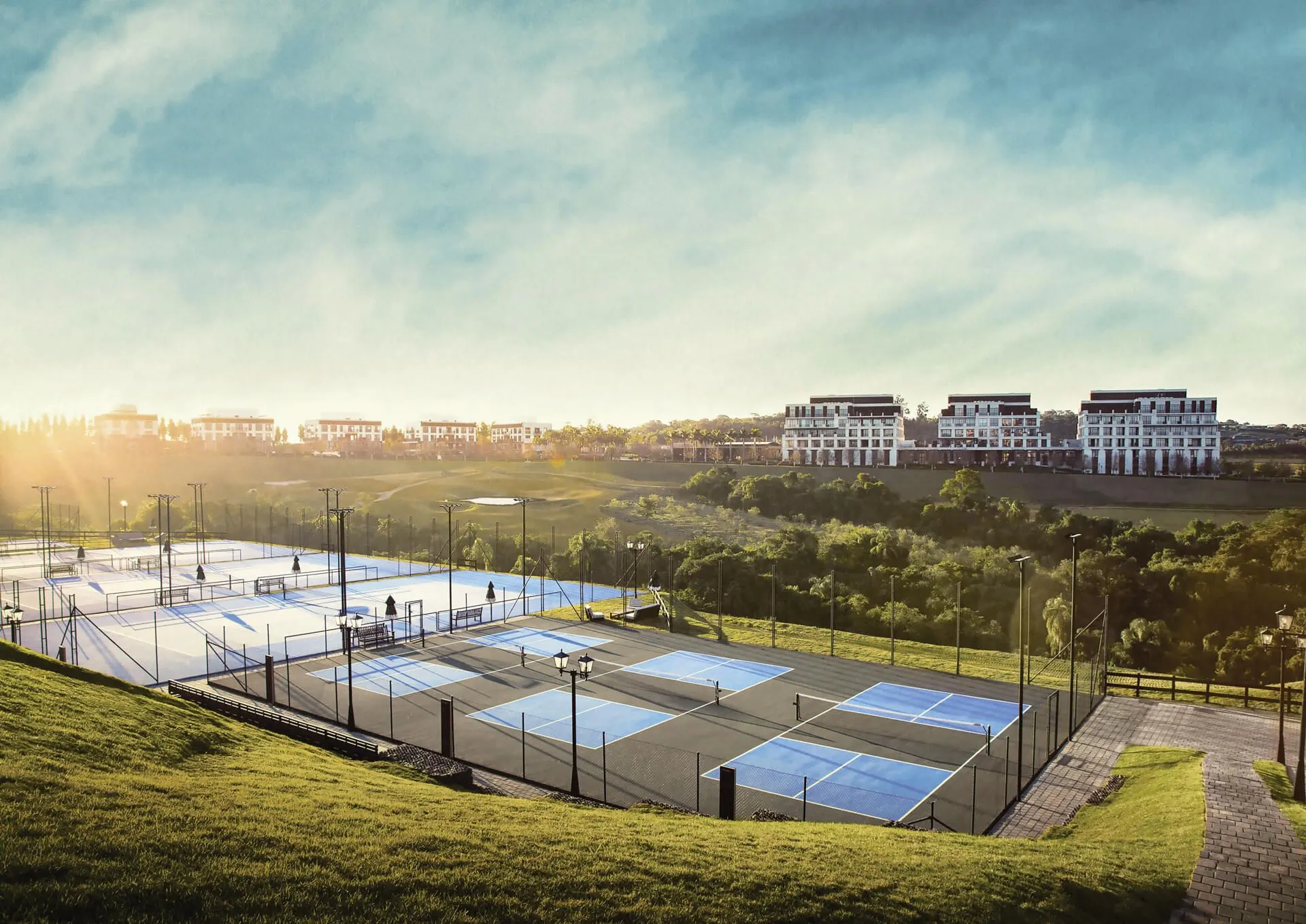 As quadras do Racquet Club ao entardecer, vistas do alto do gramado, com edifícios residenciais na linha do horizonte.