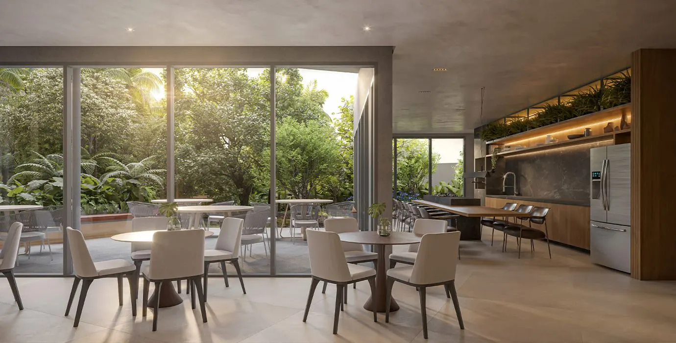 O espaço gourmet com mesas e cadeiras claras, a cozinha ao fundo e a parede de vidro aberta para o jardim.