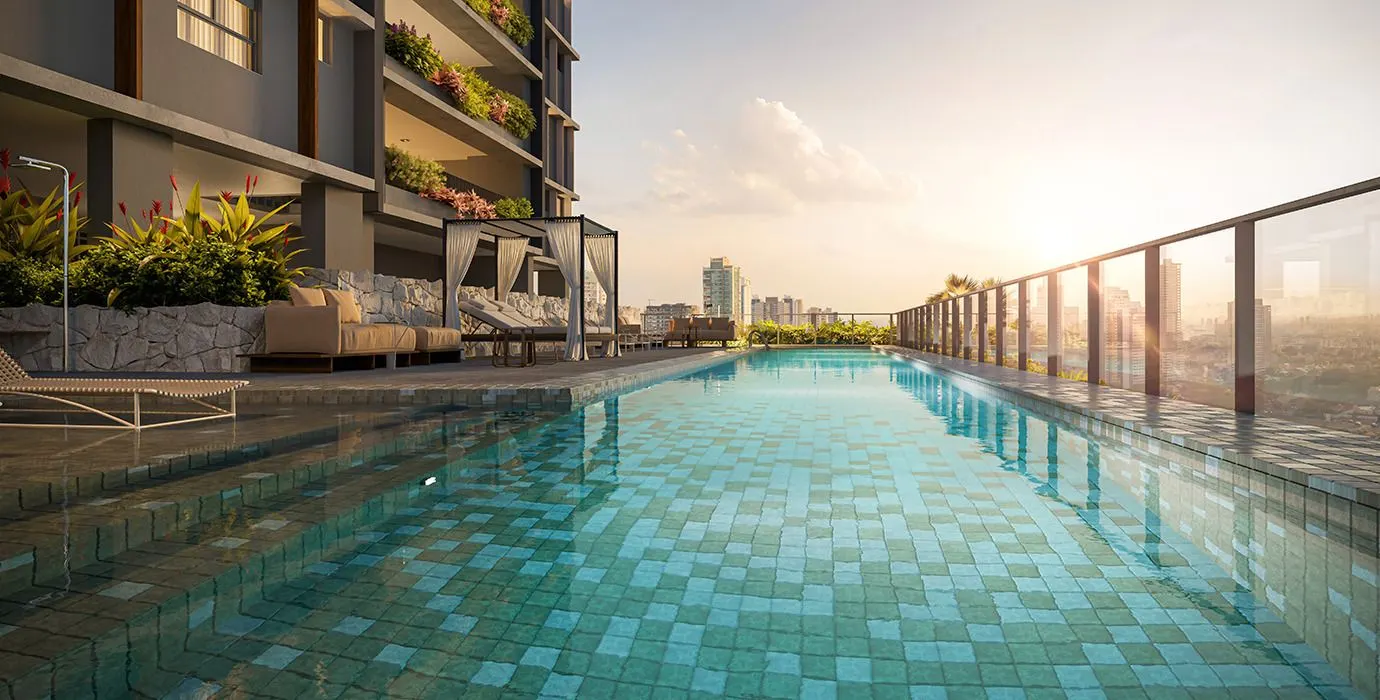 A piscina com raia ao longo do guarda-corpo de vidro, com espreguiçadeiras e a cidade ao pôr do sol.