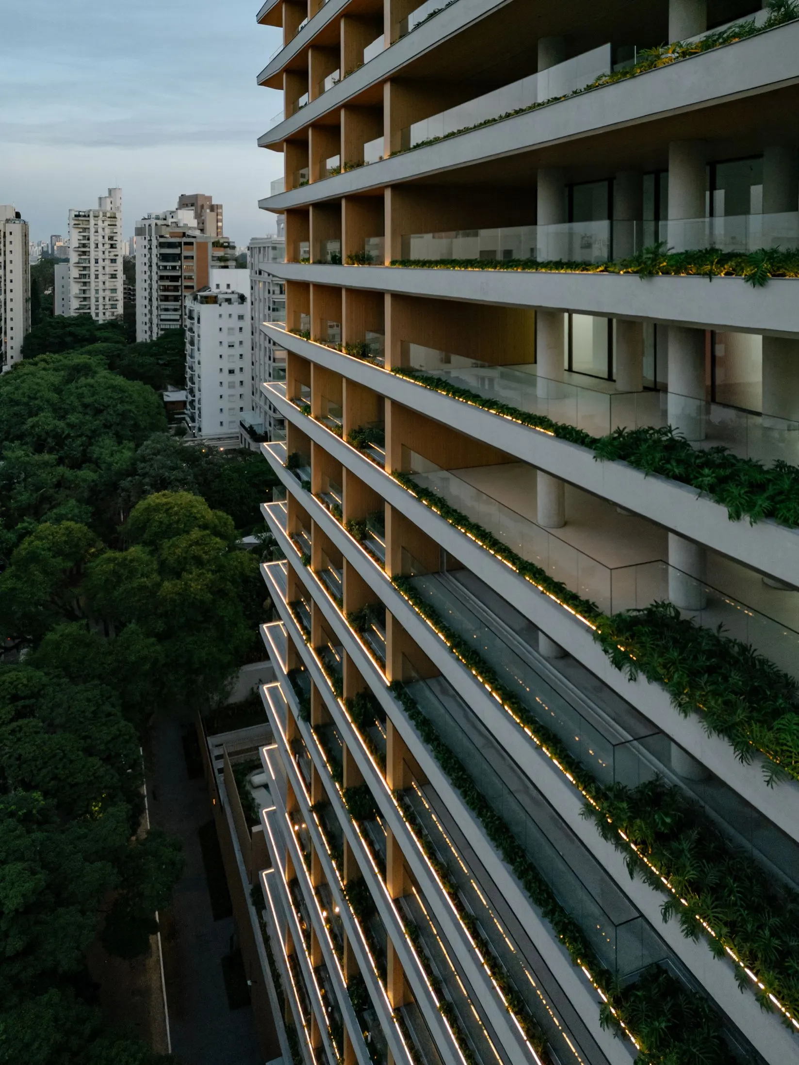 A fachada vista de cima, com as floreiras de cada andar descendo até as copas das árvores da rua.