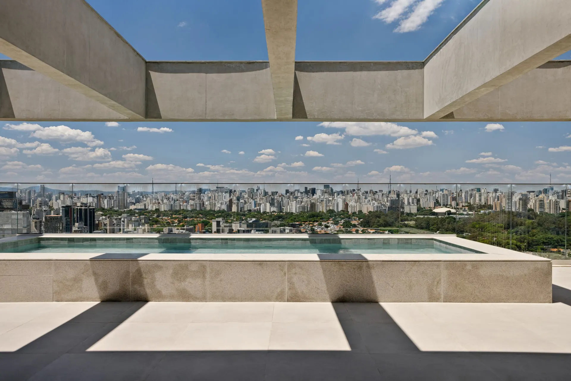 A piscina da cobertura, sob as vigas de concreto do terraço descoberto, com a cidade até o horizonte.