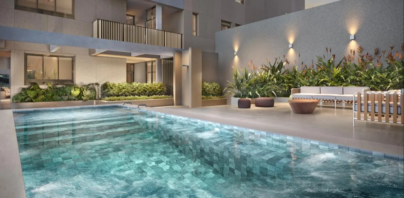 A piscina privativa do garden, revestida de pedra verde, com o deck, um sofá e floreiras tropicais junto ao muro iluminado.