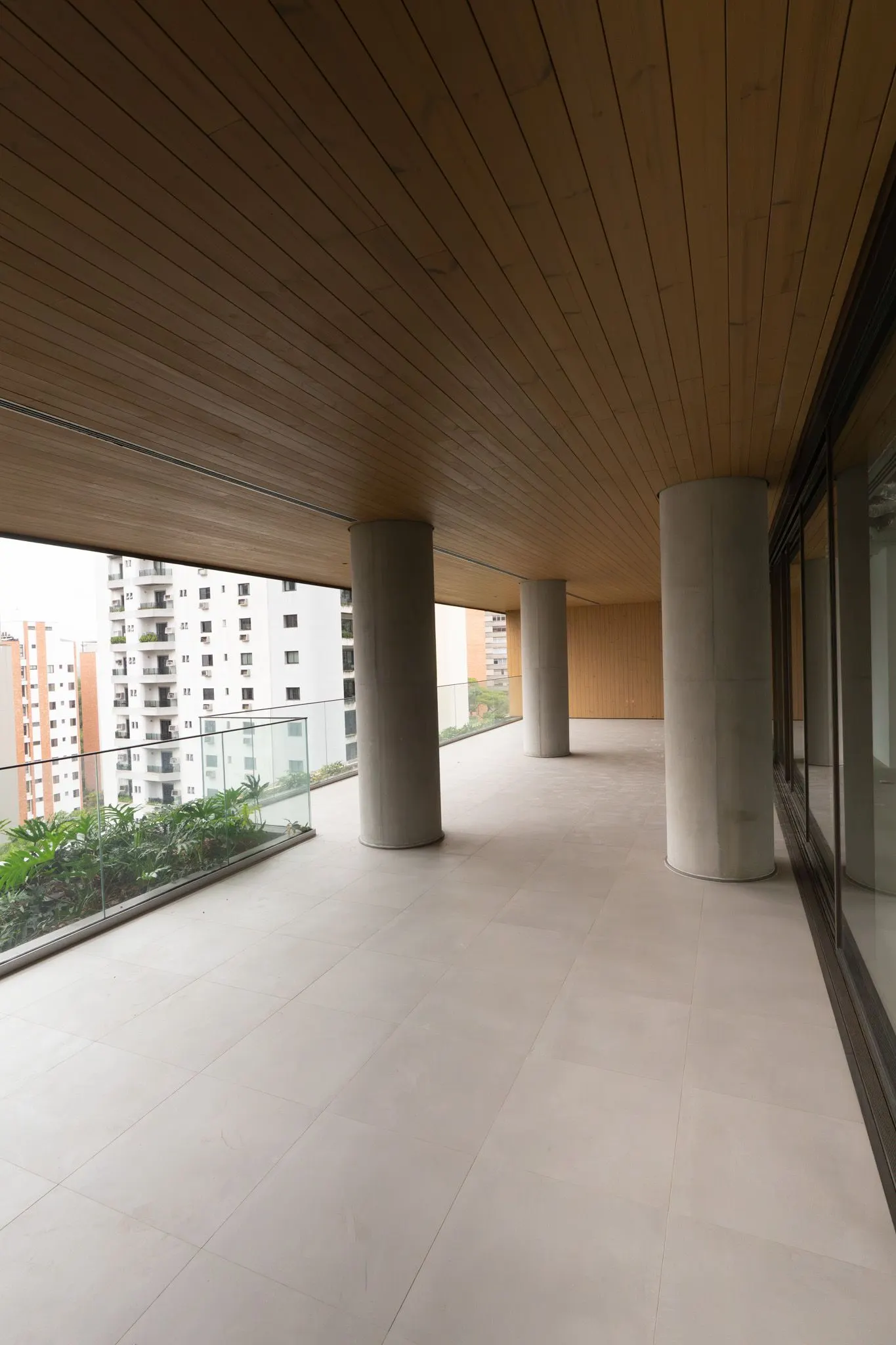 O terraço de um apartamento tipo, com forro de madeira, piso claro e a floreira, em foto do prédio pronto.