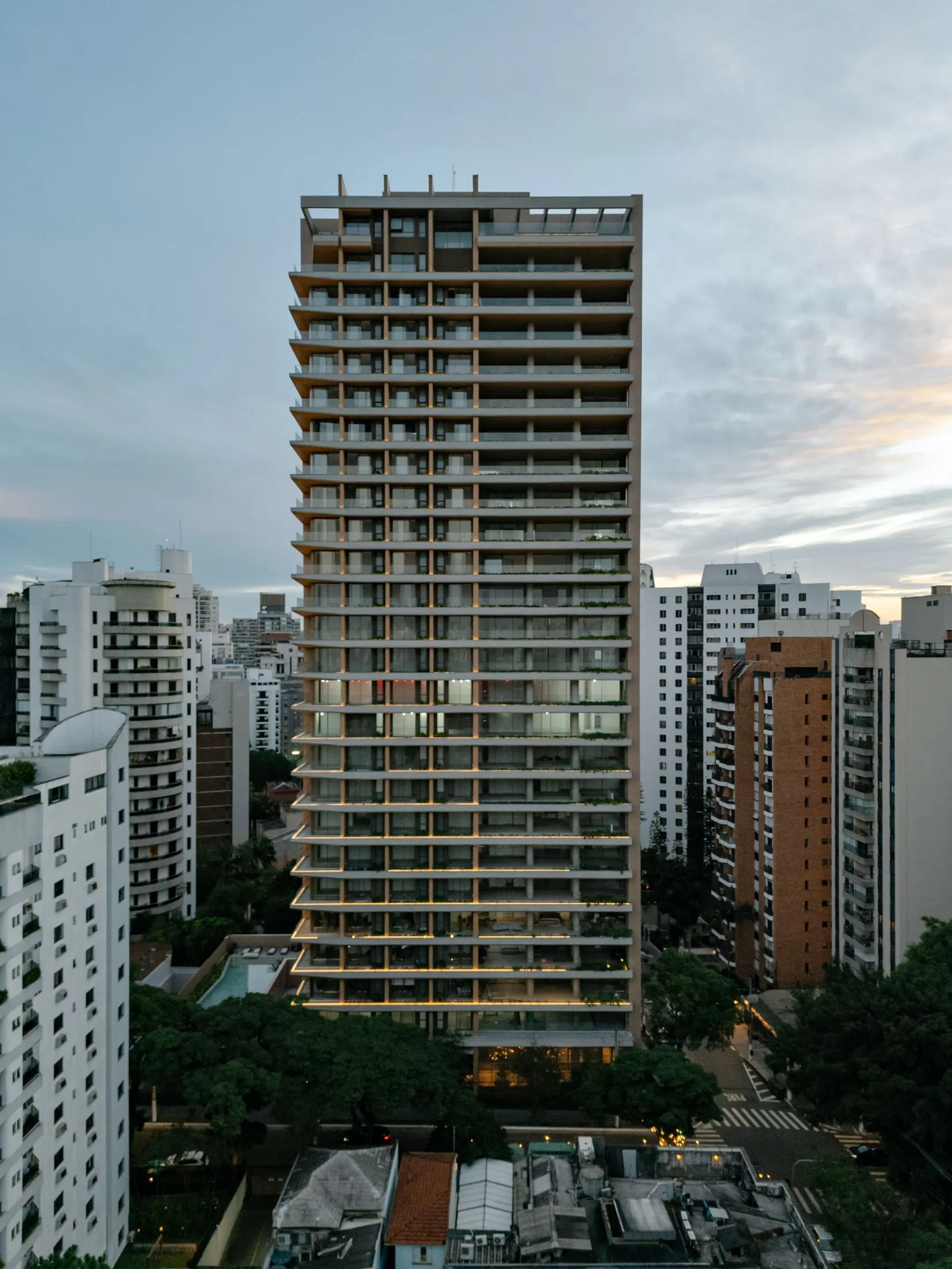 A torre do Bueno Brandão 257 ao entardecer, com as floreiras acesas, entre os prédios da Vila Nova Conceição.