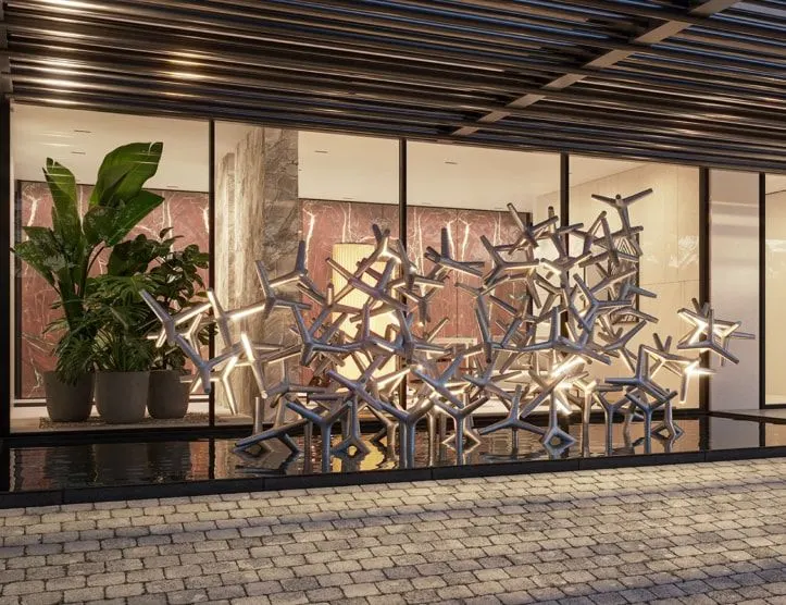 A escultura exclusiva: peças metálicas entrelaçadas atrás do vidro do lobby, entre plantas.