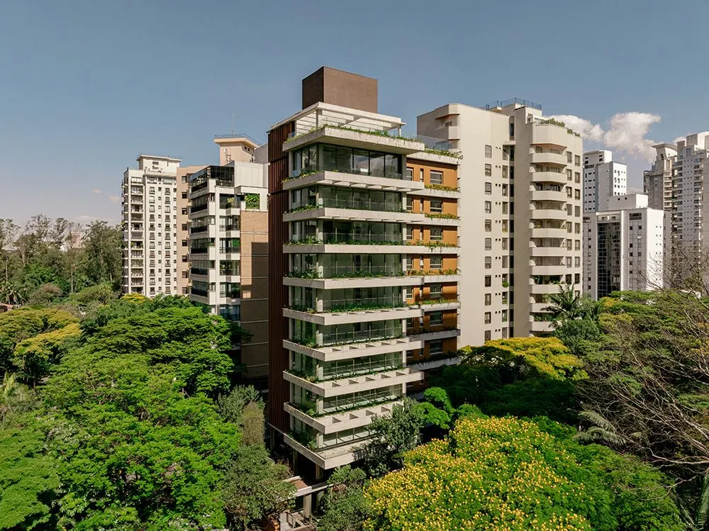 A torre da Casa Pereira Coutinho vista do alto, no meio das copas das árvores do bairro, com os prédios vizinhos em volta e o céu com nuvens.