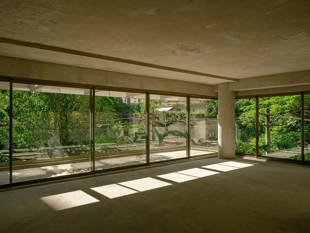 Um apartamento entregue no contrapiso, vazio: a sala com portas de vidro em dois lados, as copas das árvores lá fora e o sol desenhando retângulos no chão.