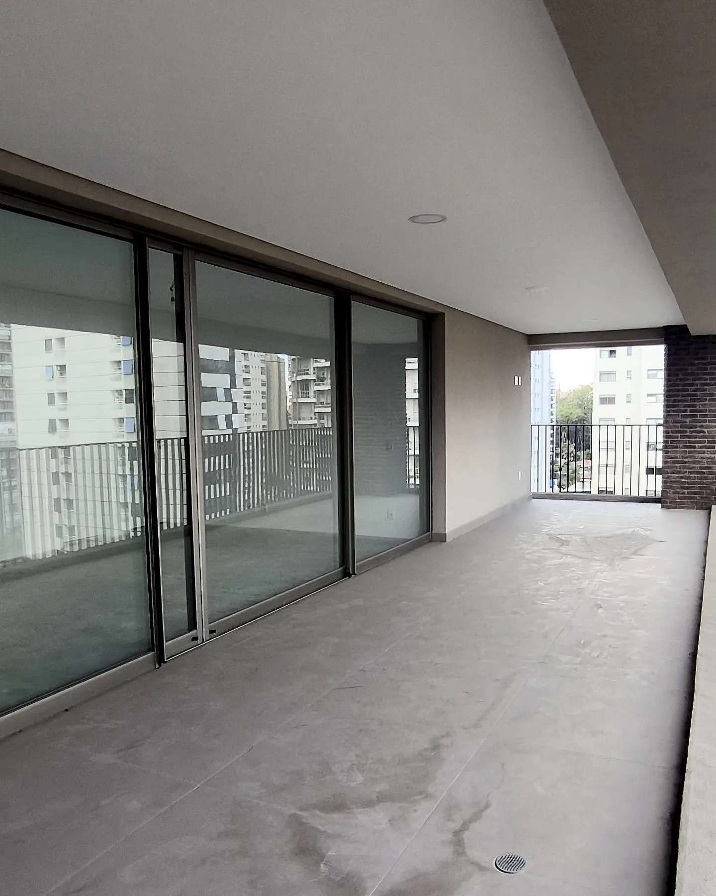 O living da unidade 102 no contrapiso: as paredes brancas e a parede de caixilhos de vidro que se abre para o terraço.
