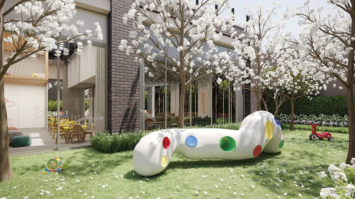 O playground no gramado, com um brinquedo branco de bolinhas coloridas sob árvores floridas.