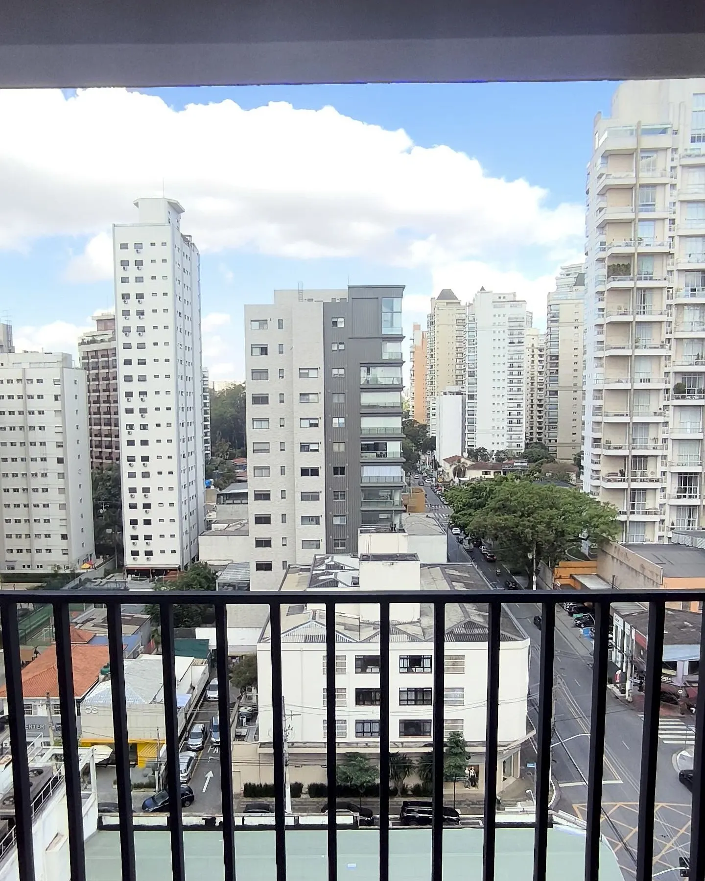 A vista do terraço da unidade 102: prédios altos da Vila Nova Conceição, copas de árvores e o céu com nuvens, atrás do guarda-corpo.