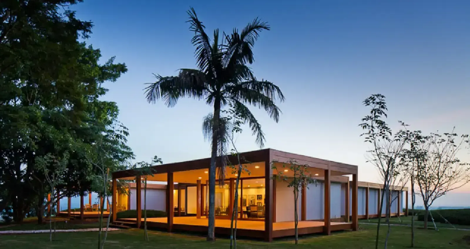 O Golf Clubhouse I, de Isay Weinfeld, aceso ao anoitecer entre as palmeiras.