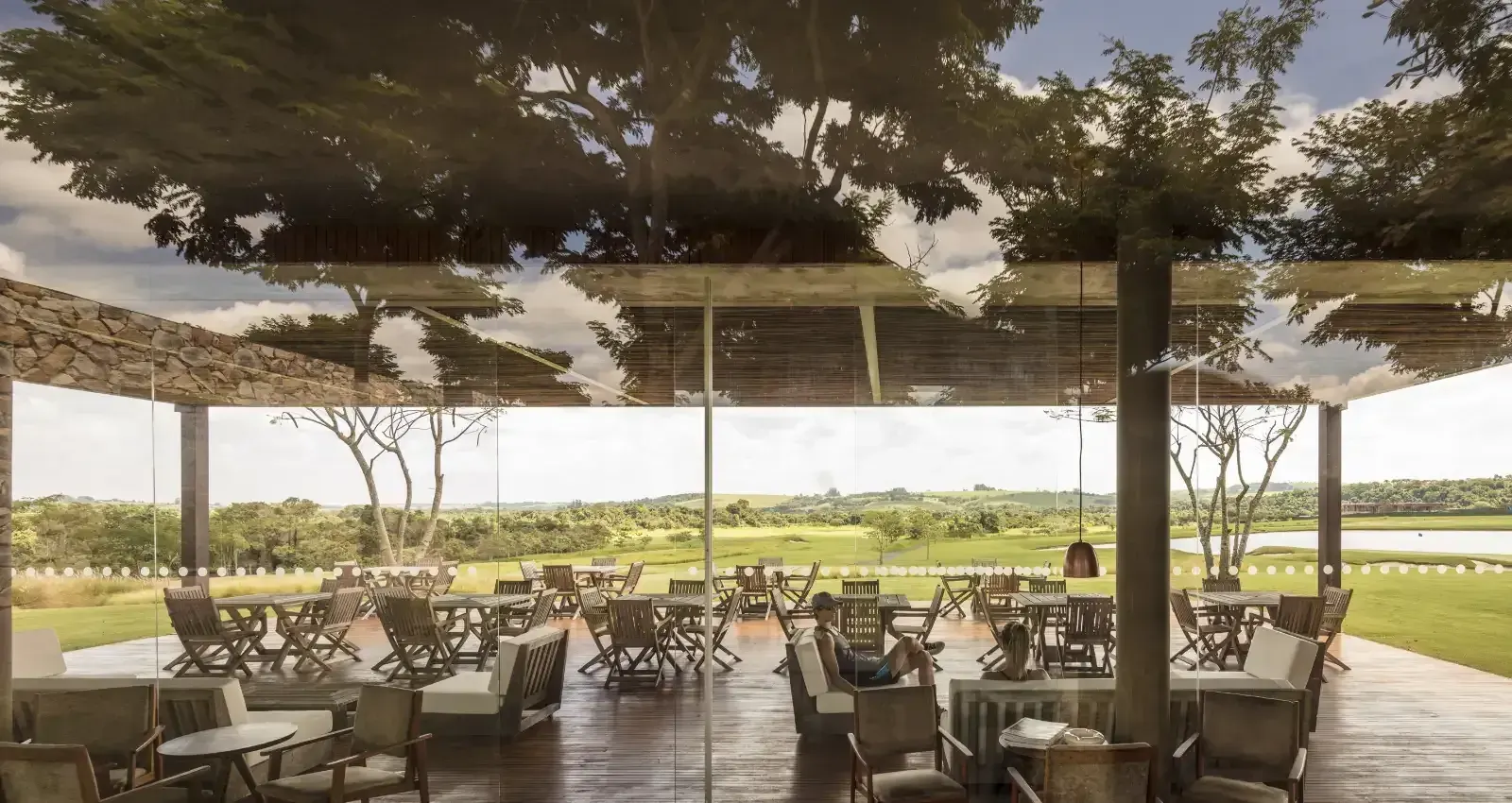 O terraço coberto do Golf Clubhouse II, com mesas voltadas para o campo.