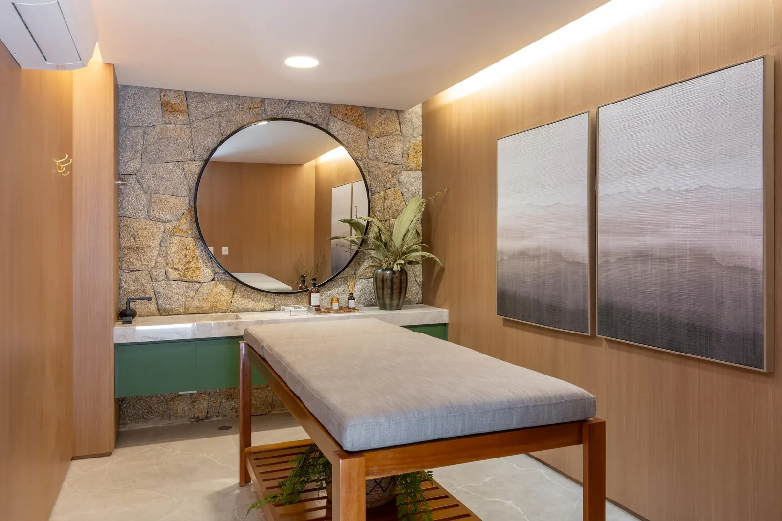 A sala de massagem: a maca de madeira, um espelho redondo sobre a parede de pedra e dois quadros em tons de névoa.