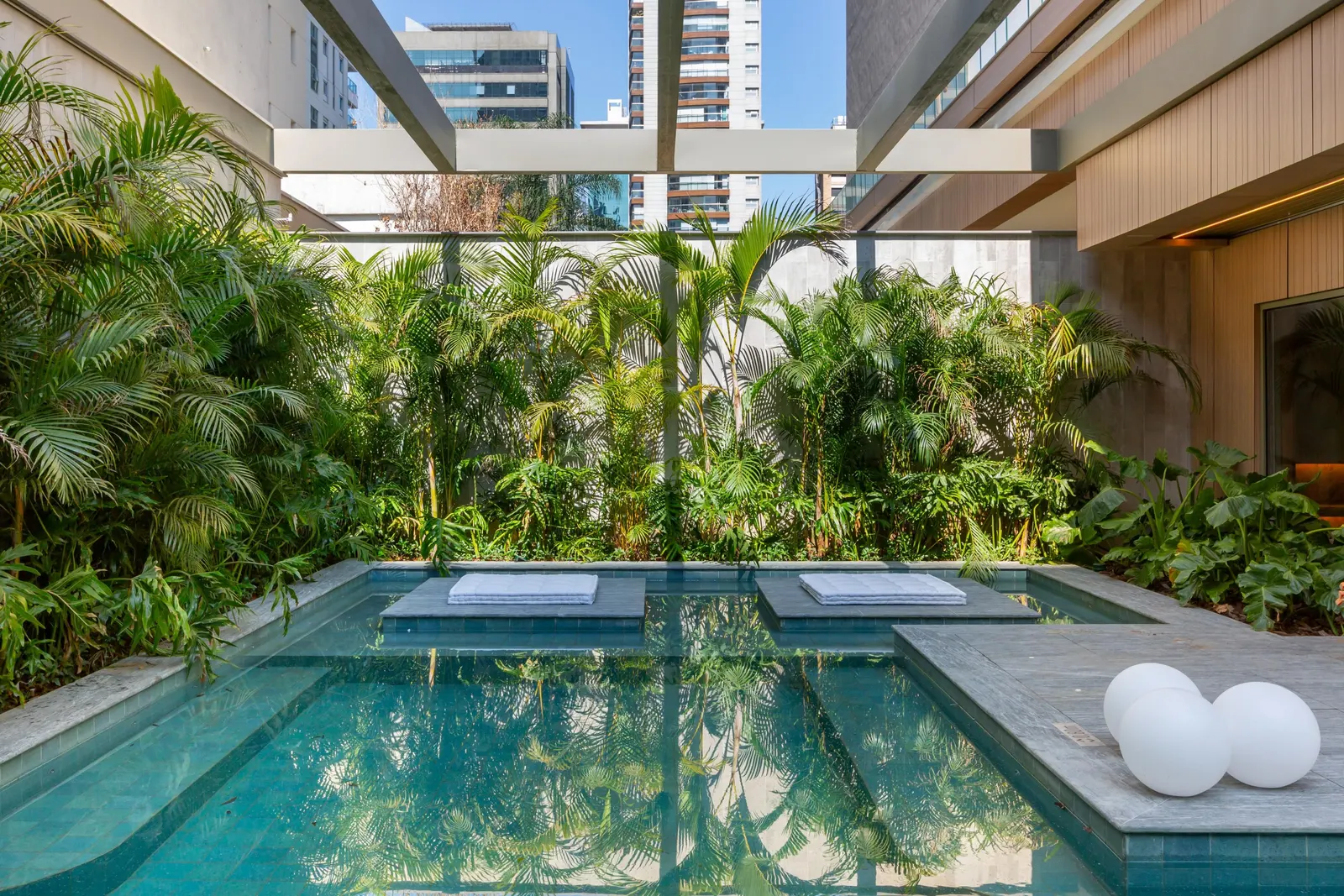 O spa: água rasa com dois colchões, esferas de luz na borda e um jardim de palmeiras fechando o fundo.