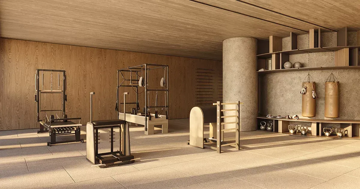 A sala de pilates: aparelhos de madeira, sacos de pancada pendurados e uma coluna de concreto, com a luz entrando de lado.