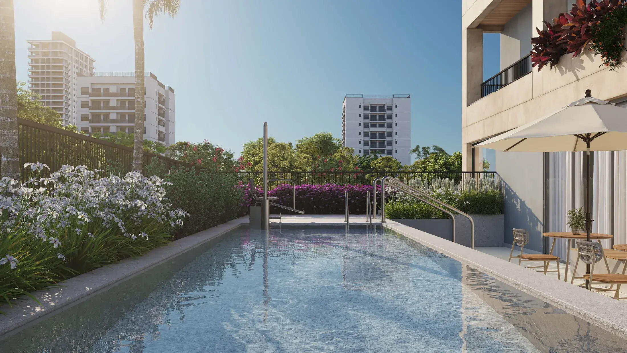 A piscina descoberta do 1º pavimento: a raia ao longo do jardim florido, o guarda-sol e as espreguiçadeiras, os prédios do bairro ao fundo.