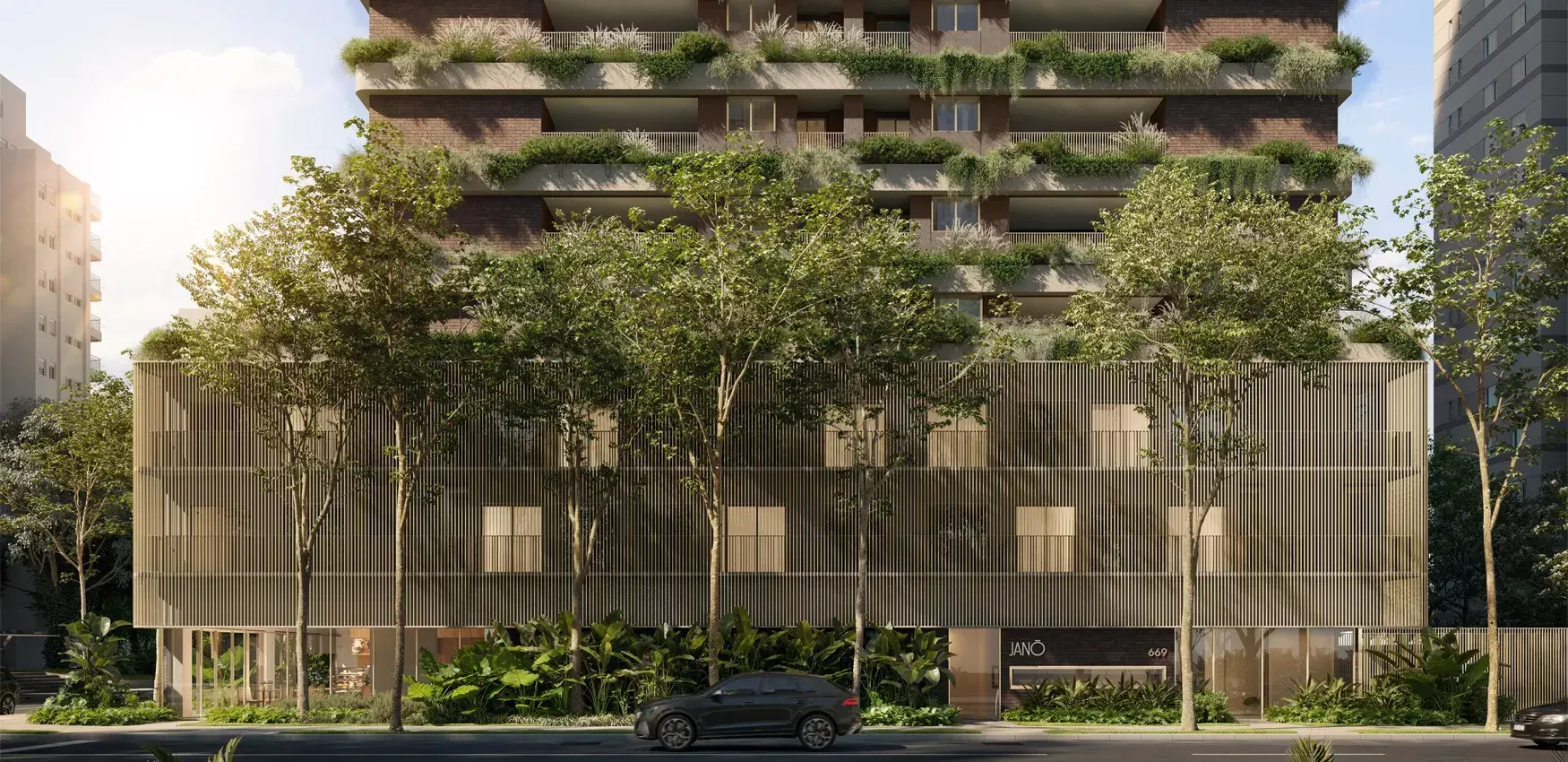 O embasamento do Janô visto da rua: o muro de ripas claras entre árvores e jardins na calçada, e as primeiras varandas verdes acima.