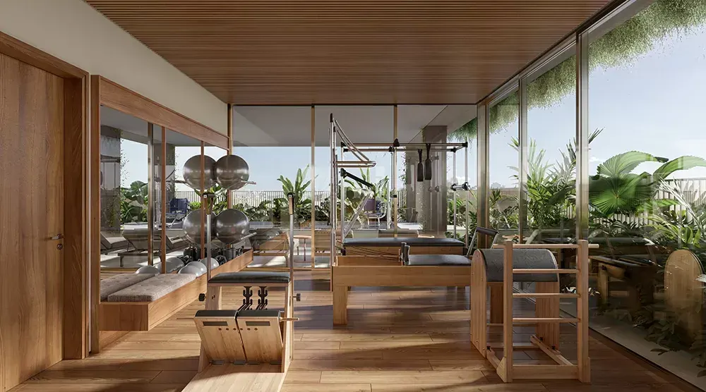 O studio de pilates com os aparelhos de madeira, piso claro e janelas para as árvores.