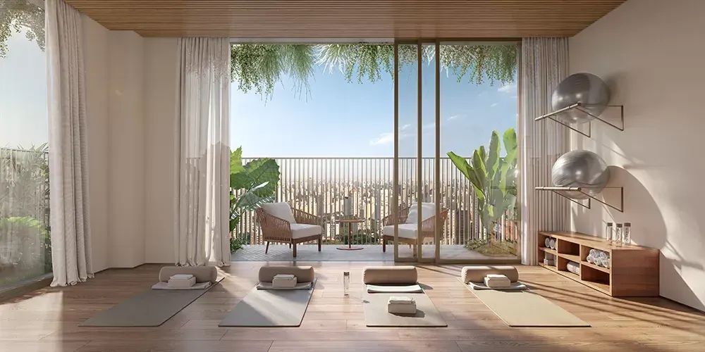 A sala de yoga com piso de madeira, tapetes e bolas, aberta por portas de vidro para um jardim de folhagens.