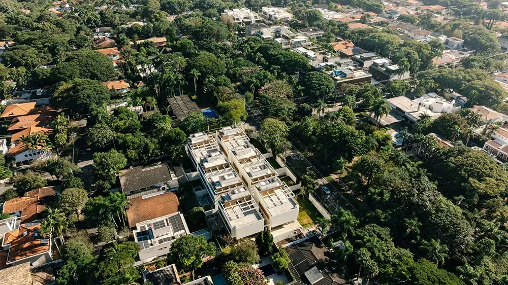 O condomínio visto do alto: as casas brancas com os rooftops no meio das copas das árvores do Alto de Pinheiros, e as ruas e casas do bairro em volta.