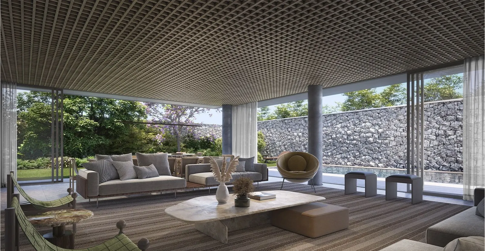 Perspectiva do living de uma casa decorado: sofás claros sobre um tapete grande, o forro de madeira e a parede de vidro aberta para o jardim, com um muro de pedra ao fundo.