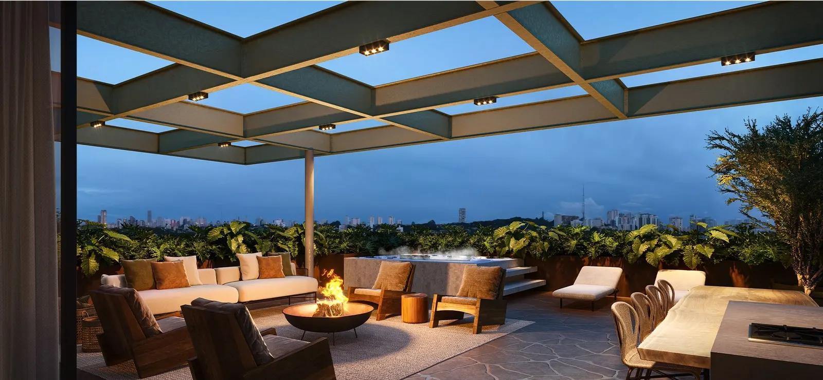 Perspectiva do rooftop decorado ao anoitecer: poltronas em volta de uma lareira baixa, a pérgula sobre elas e as luzes da cidade no horizonte.