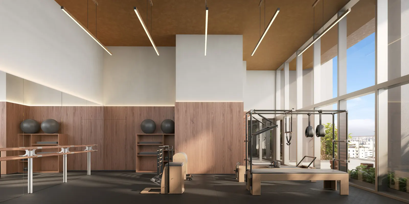 O estúdio de pilates: os aparelhos sobre o piso de madeira, sob o forro claro, com a parede de vidro.