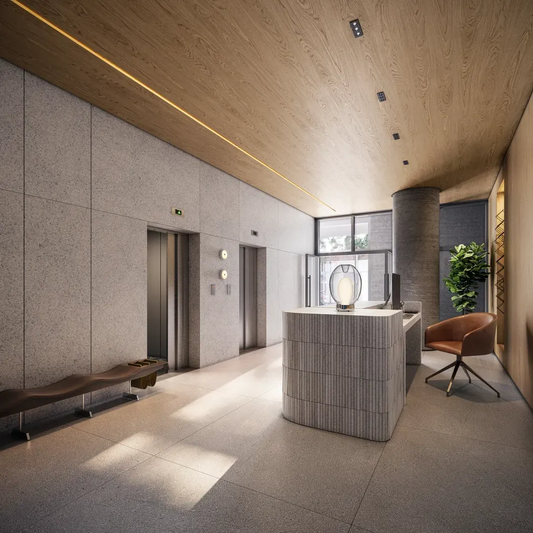 O lobby dos studios: o balcão de pedra clara sob a luz embutida, o forro de madeira, os elevadores ao fundo e uma poltrona laranja.