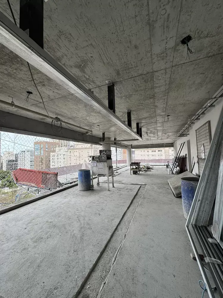 Um pavimento em obra, aberto de ponta a ponta: o piso de concreto, a laje sem forro e a fachada ainda sem caixilhos, com os prédios do bairro do lado de fora.