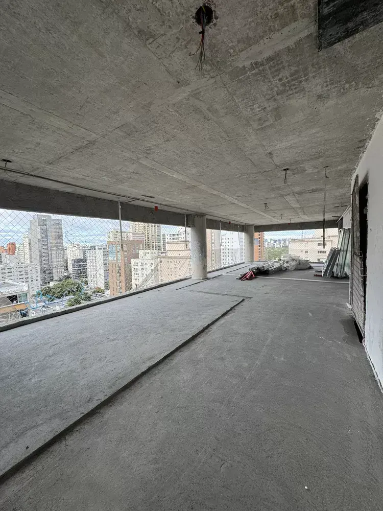 Um pavimento largo em obra, com a laje de concreto aparente e as aberturas da fachada para os prédios vizinhos e o céu.