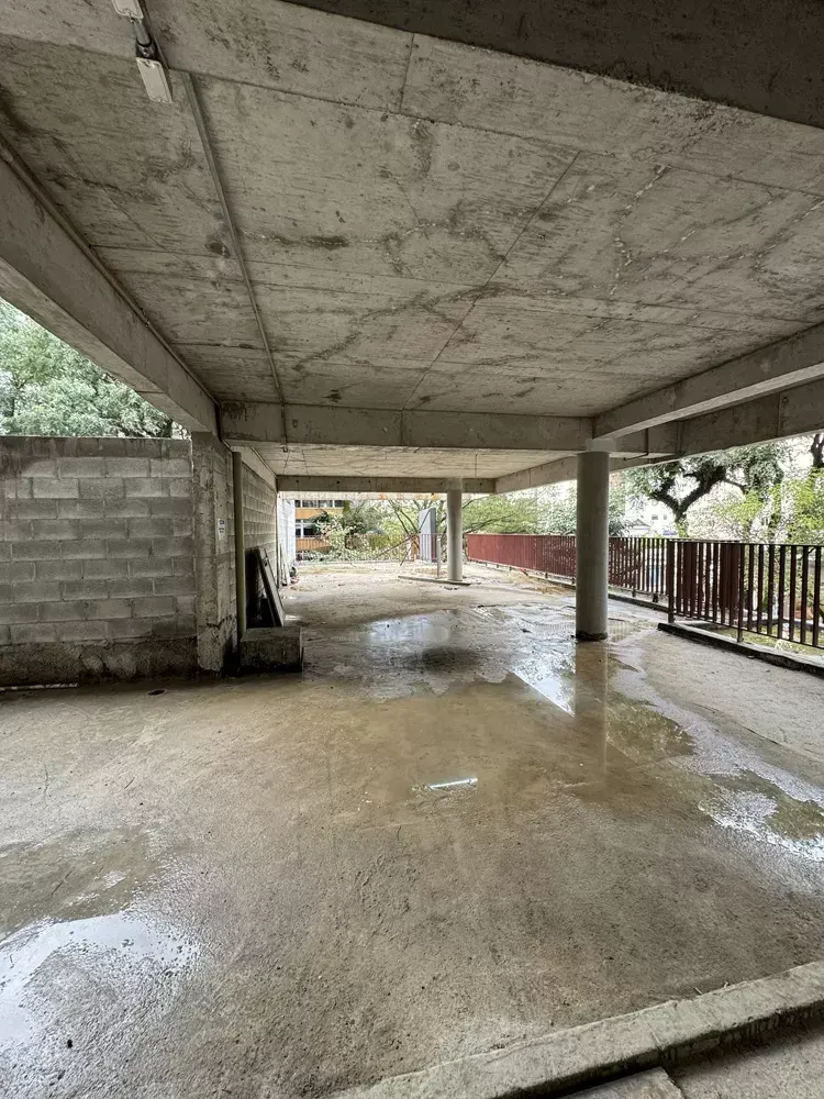 O térreo em obra: a laje apoiada nos pilares, o piso molhado e o muro de blocos ao fundo, com as árvores do lado de fora.