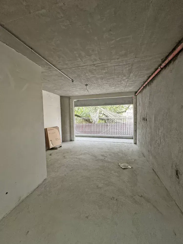 Um ambiente com as paredes levantadas e rebocadas, o teto de concreto e a janela para os prédios do bairro.
