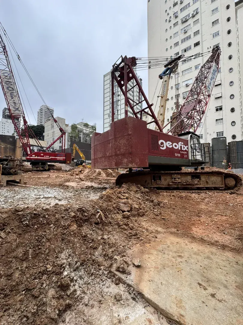 Uma máquina de fundação vermelha sobre a terra, ao lado dos prédios altos da rua.