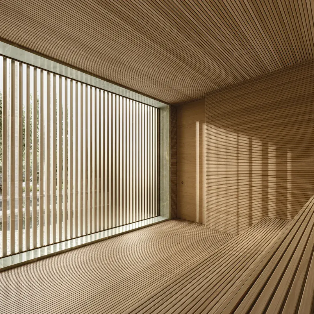 A sauna seca: os bancos de madeira clara em degraus e a parede de ripas com a luz que entra entre elas.
