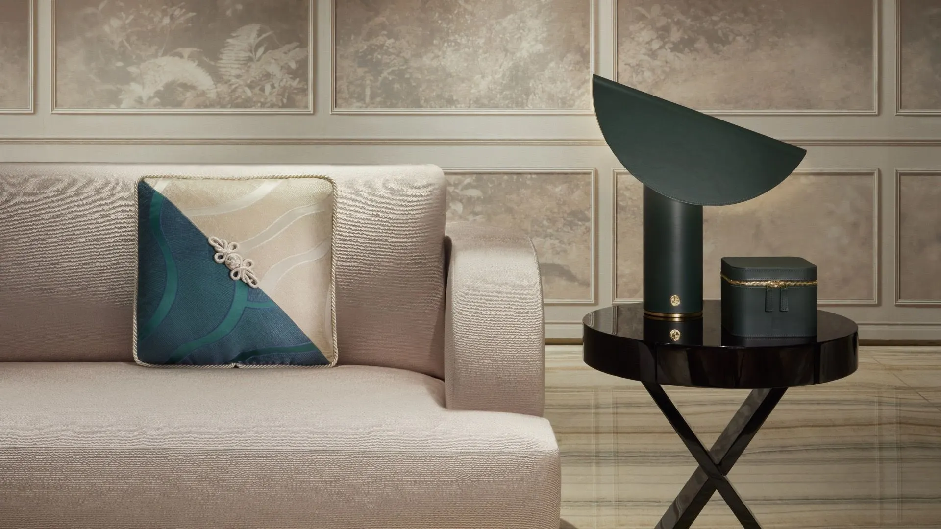 Detalhe Armani/Casa: sofá claro com almofada de seda em azul e bege, e uma luminária escura sobre mesa lateral.