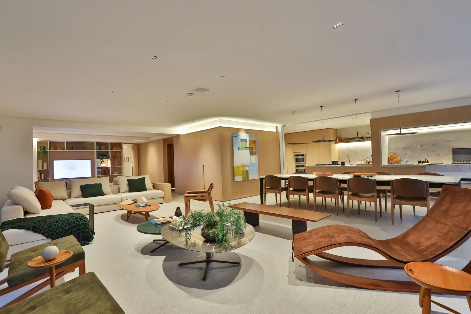 O living do decorado de ponta a ponta: o estar com chaise de couro e poltronas verdes em primeiro plano, a mesa de jantar e a cozinha de madeira ao fundo.